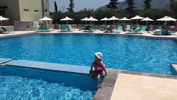 A swimming pool with lounge chairs and umbrellas, surrounded by a stone wall and trees.
