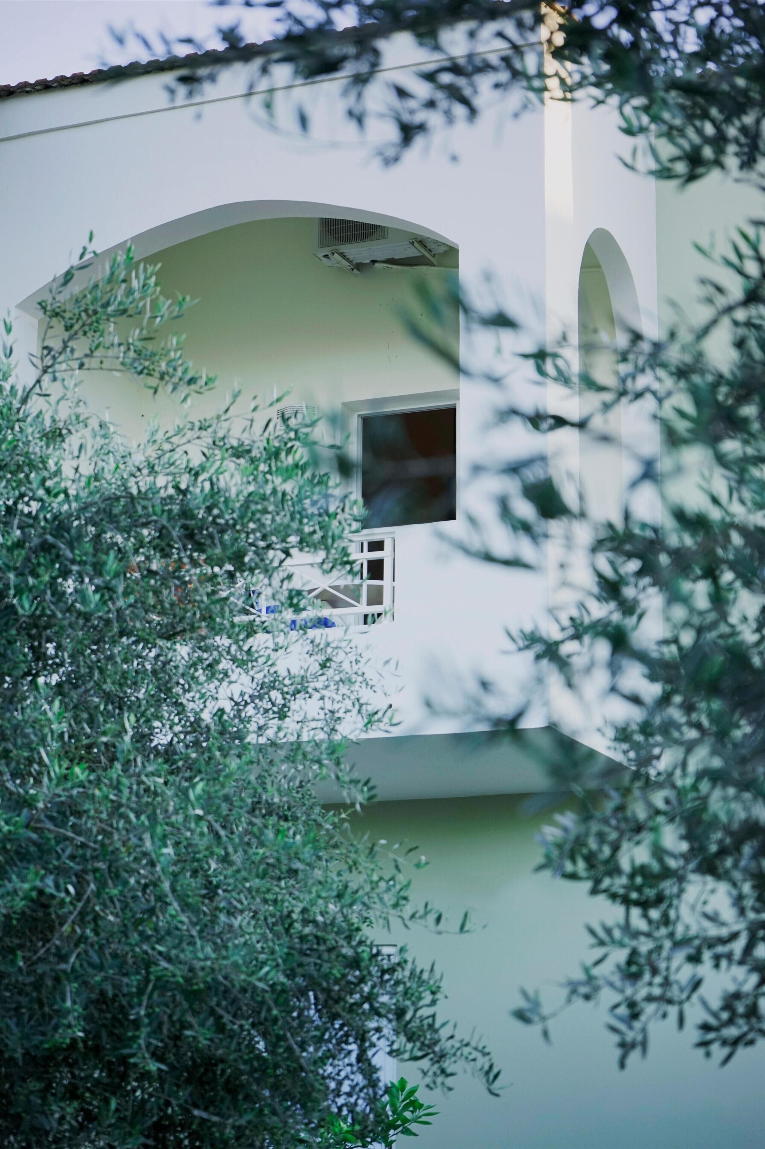 Un edificio con fachada blanca, una ventana de estructura metálica y un pequeño balcón.