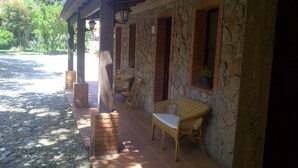 A covered outdoor seating area with wicker furniture, stone walls, and a brick floor. - Agriturismo La Quercia (Arbus)