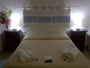 A neatly made bed with towels and toiletries, two bedside tables with lamps, and a floral arrangement on one table. - Agriturismo La Quercia (Arbus)