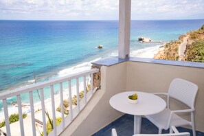 Un balcón con vista al océano, una mesa blanca y una silla blanca.