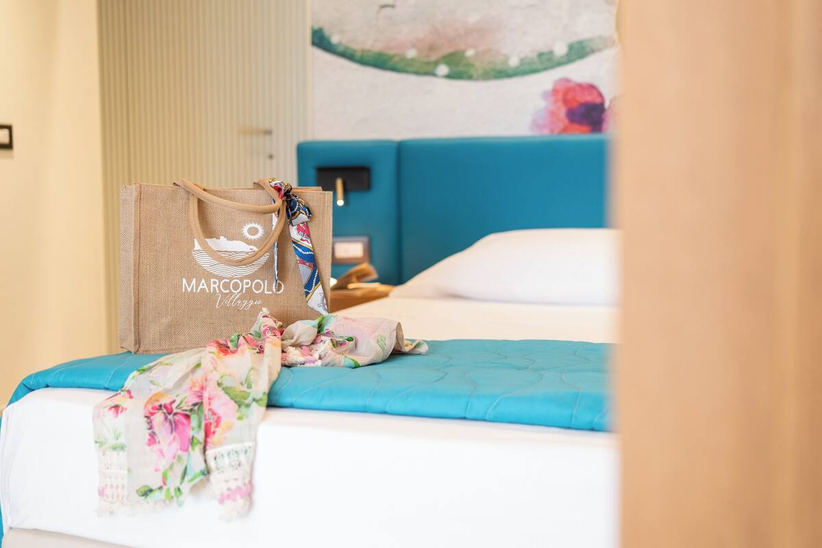 A bed with a blue headboard, a floral-patterned blanket, and a burlap bag with text.