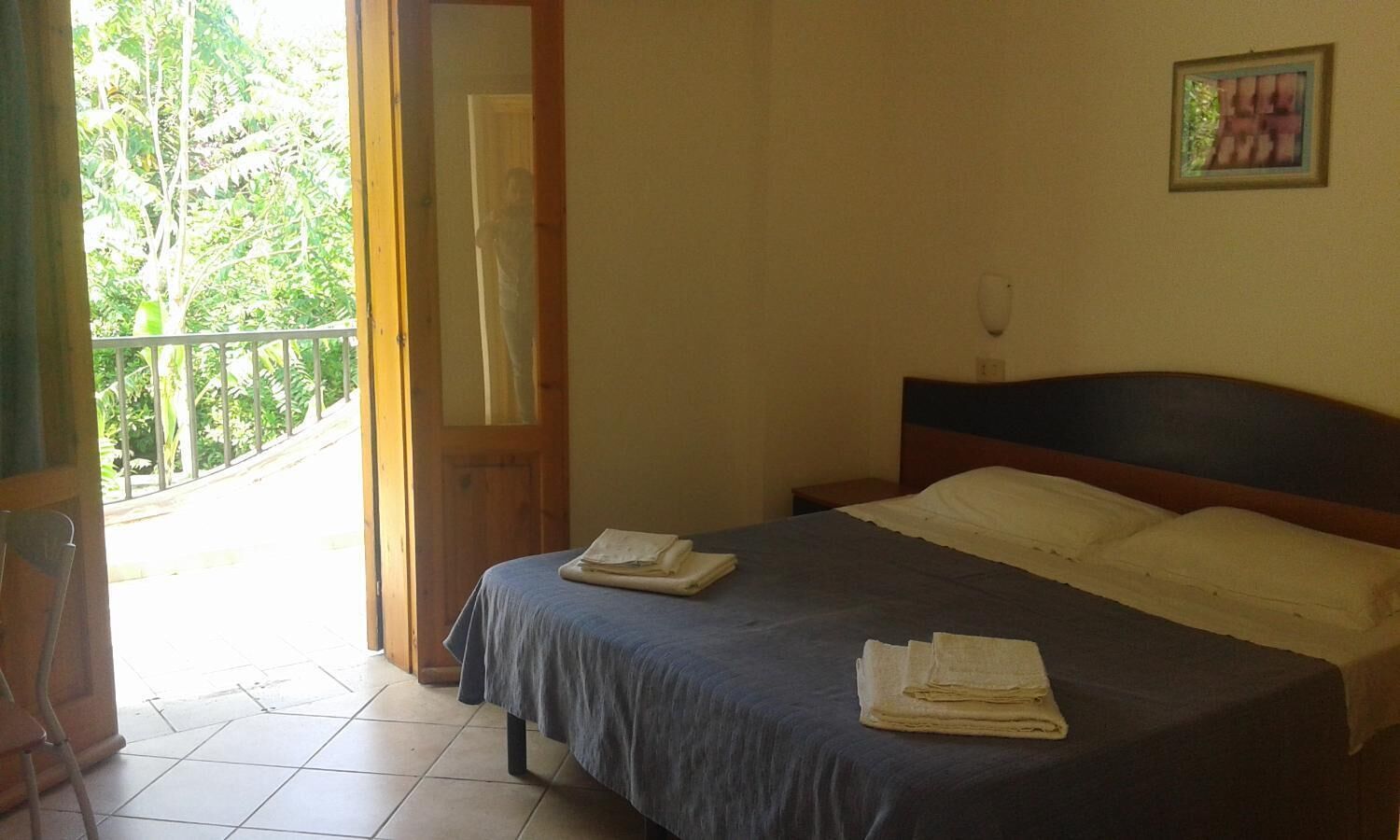 Une chambre à coucher avec un lit, une tête de lit en bois, une table de chevet et une fenêtre donnant sur des arbres.