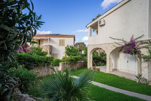 Un patio con un edificio blanco, un muro de piedra y abundante vegetación.