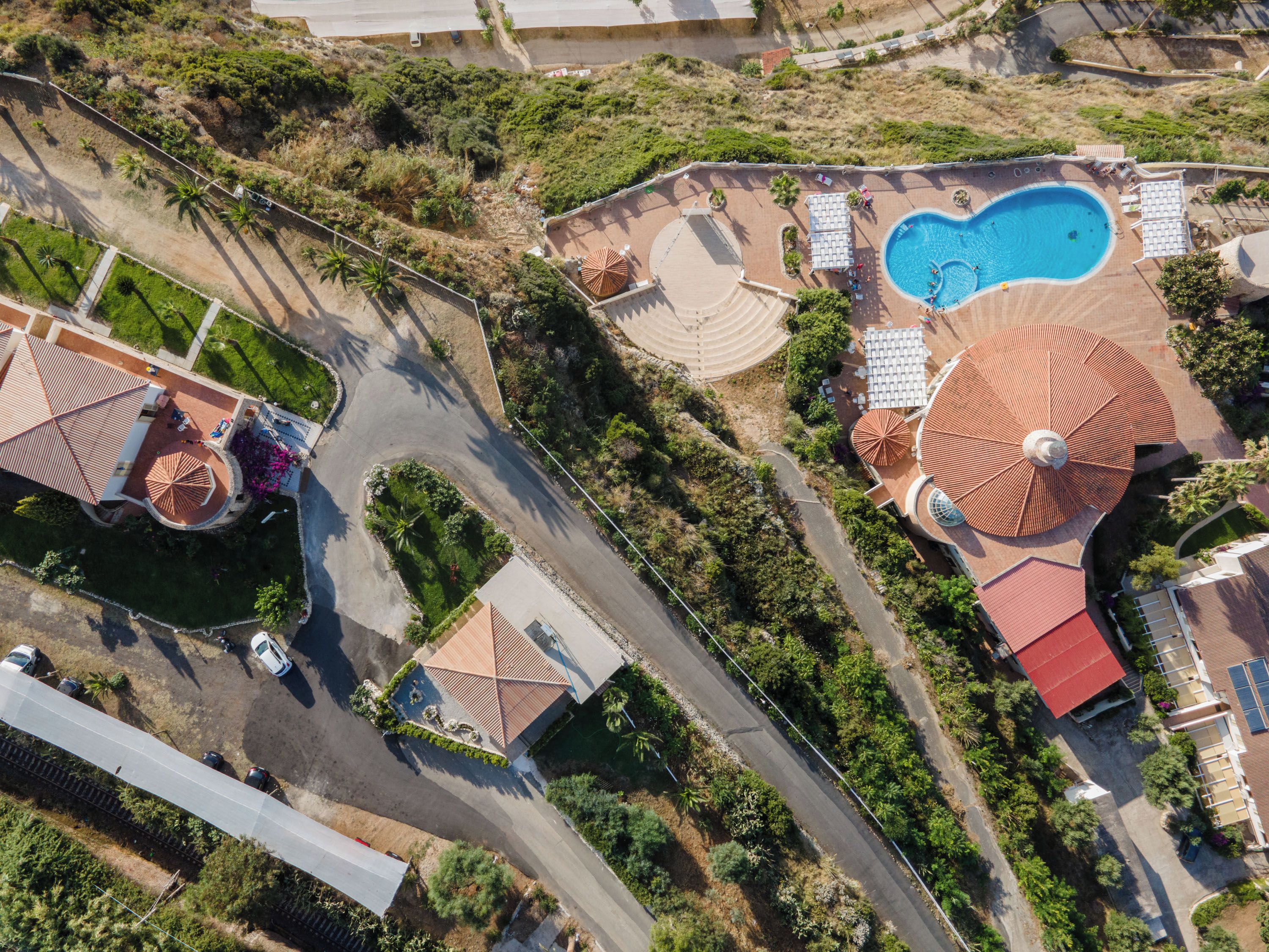 Vista aérea de un complejo turístico con piscina, sombrillas y una zona de estacionamiento.