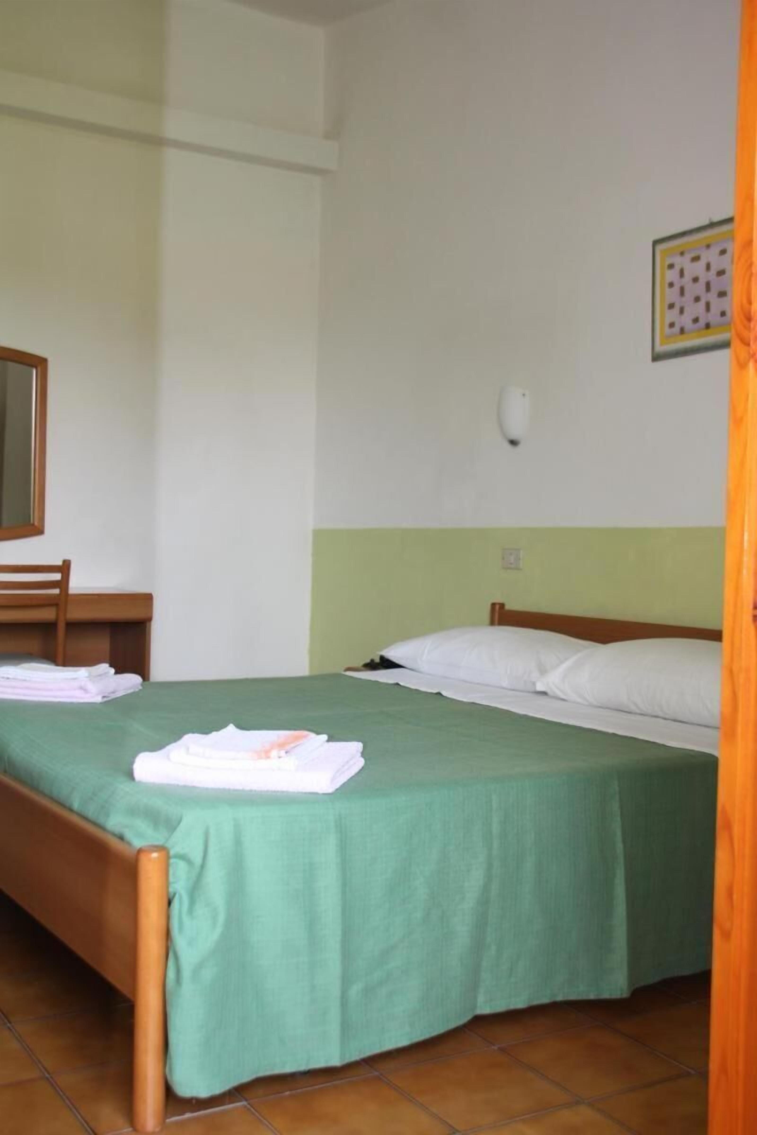 A single bed with a green bedspread, a wooden headboard, and a wooden nightstand with a mirror.