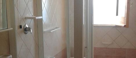 Et badeværelse med brusekabine med glasvægge, vask og toilet.