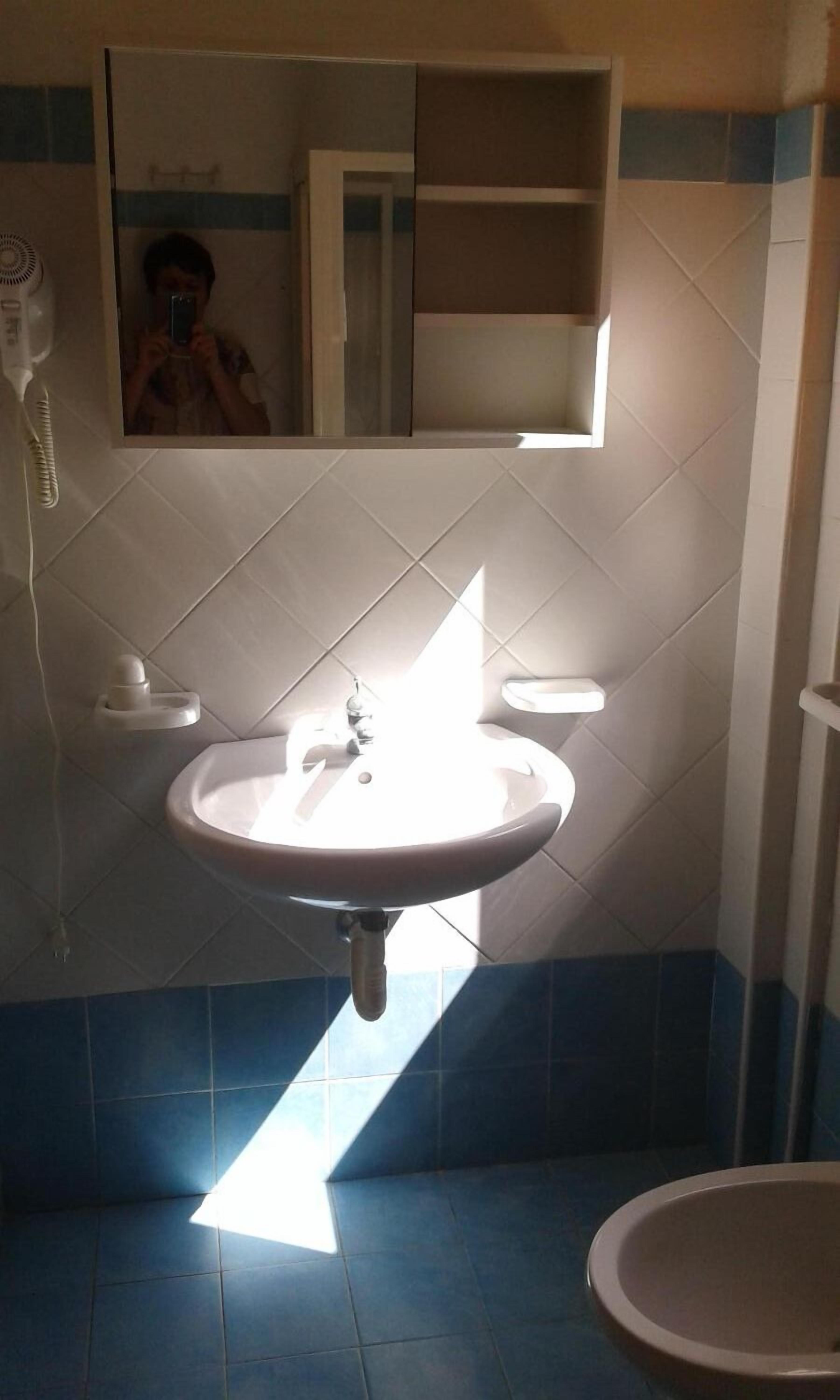 A bathroom with a white sink, a mirror, and a toilet. There is a towel rack on the wall and a shelf above the sink.