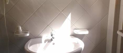 A bathroom with a white sink, a mirror, and a toilet. There is a towel rack on the wall and a shelf above the sink.
