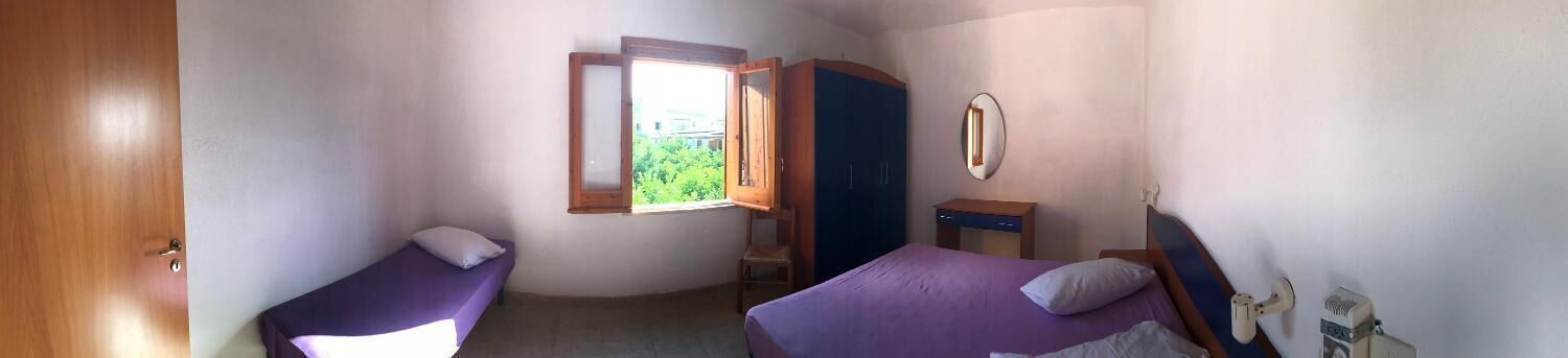 A small bedroom with two beds, a window, a wardrobe, and a mirror.
