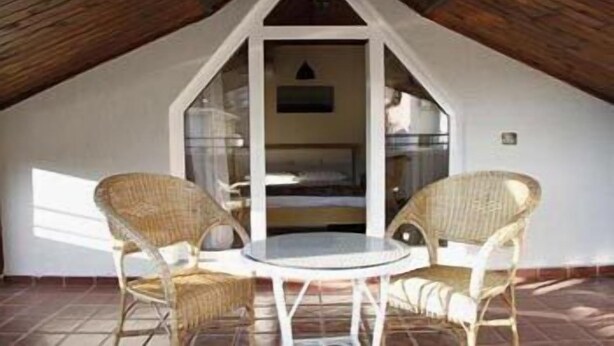 Pequeño patio amurallado con dos sillas de mimbre y una mesa redonda, con techo inclinado y vista al interior.