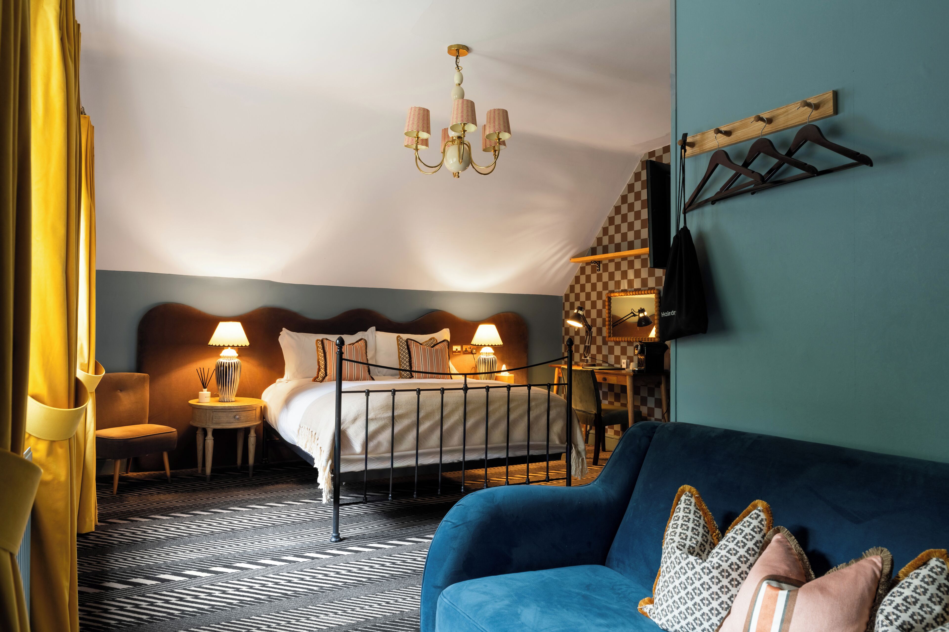 Habitación de hotel con cama, sofá azul, candelabro, televisor y pared a cuadros.