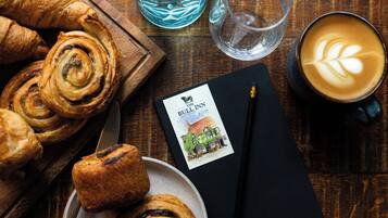 A wooden table with pastries, a coffee cup, a notebook, and a pen.