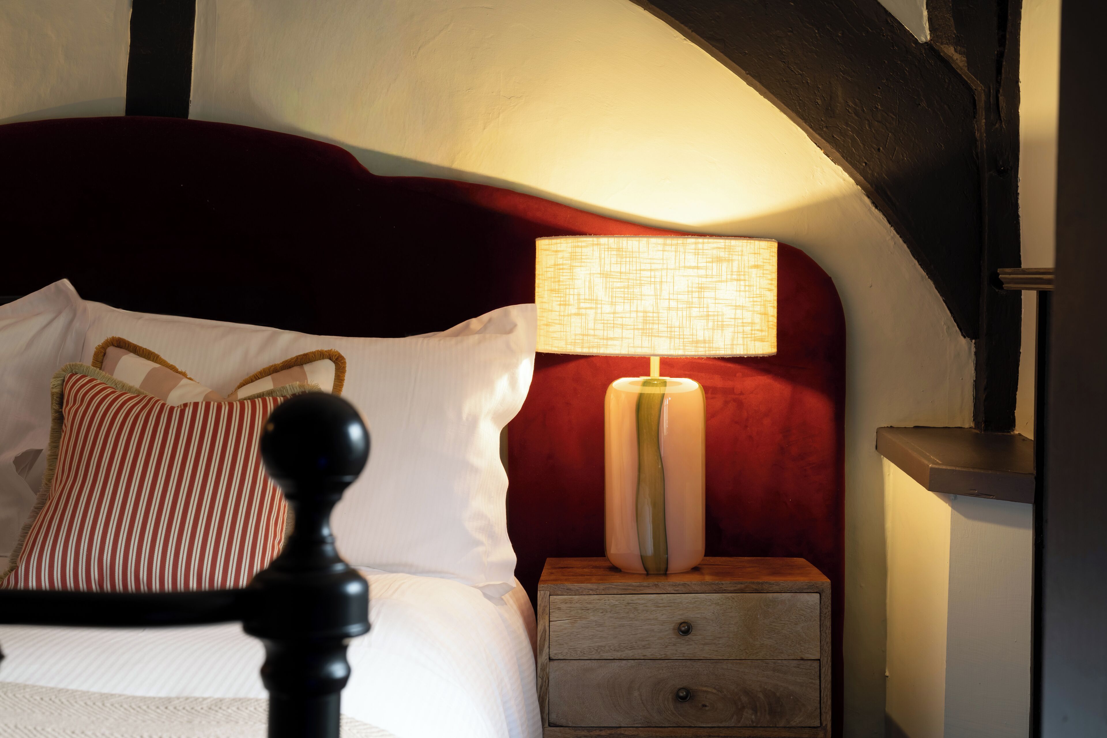 A bedroom with a bed, a nightstand, a lamp, and a wooden headboard.
