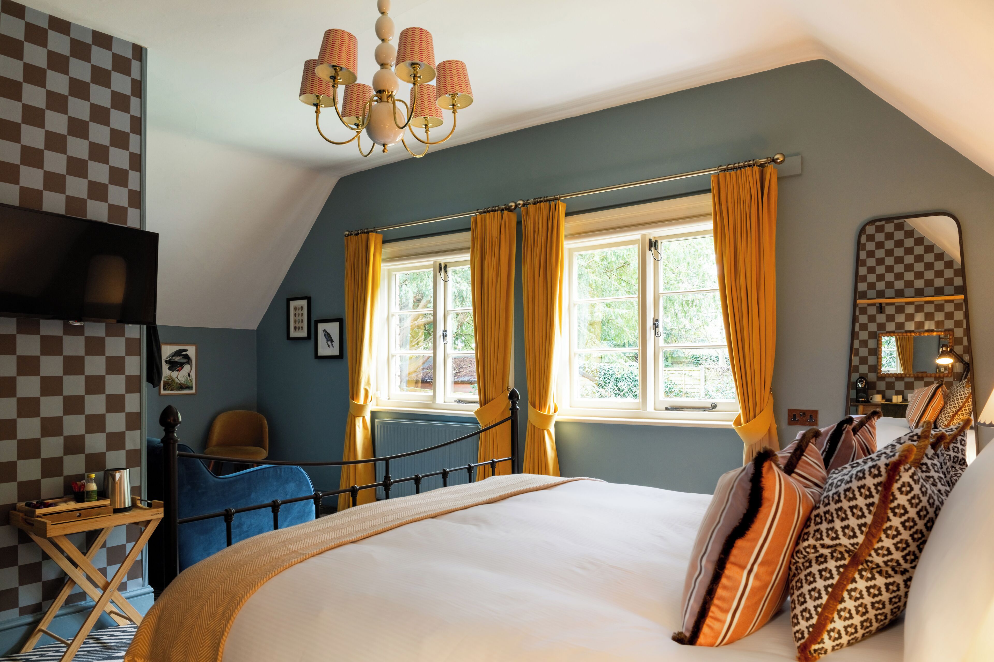 A bedroom with a bed, a chair, a window with curtains, a chandelier, and a checkered wall.