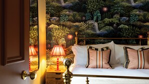 Un dormitorio con cama, almohadas, una mesita de noche, una lámpara y un mural en la pared.