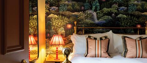 A bedroom with a bed, pillows, a nightstand, a lamp, and a wall mural.