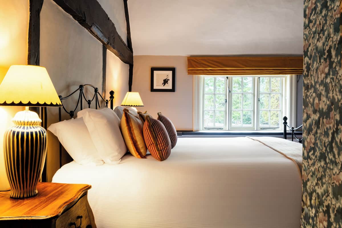 Quarto com cama grande, duas luminárias de cabeceira, janela com vista para árvores e quadro na parede.