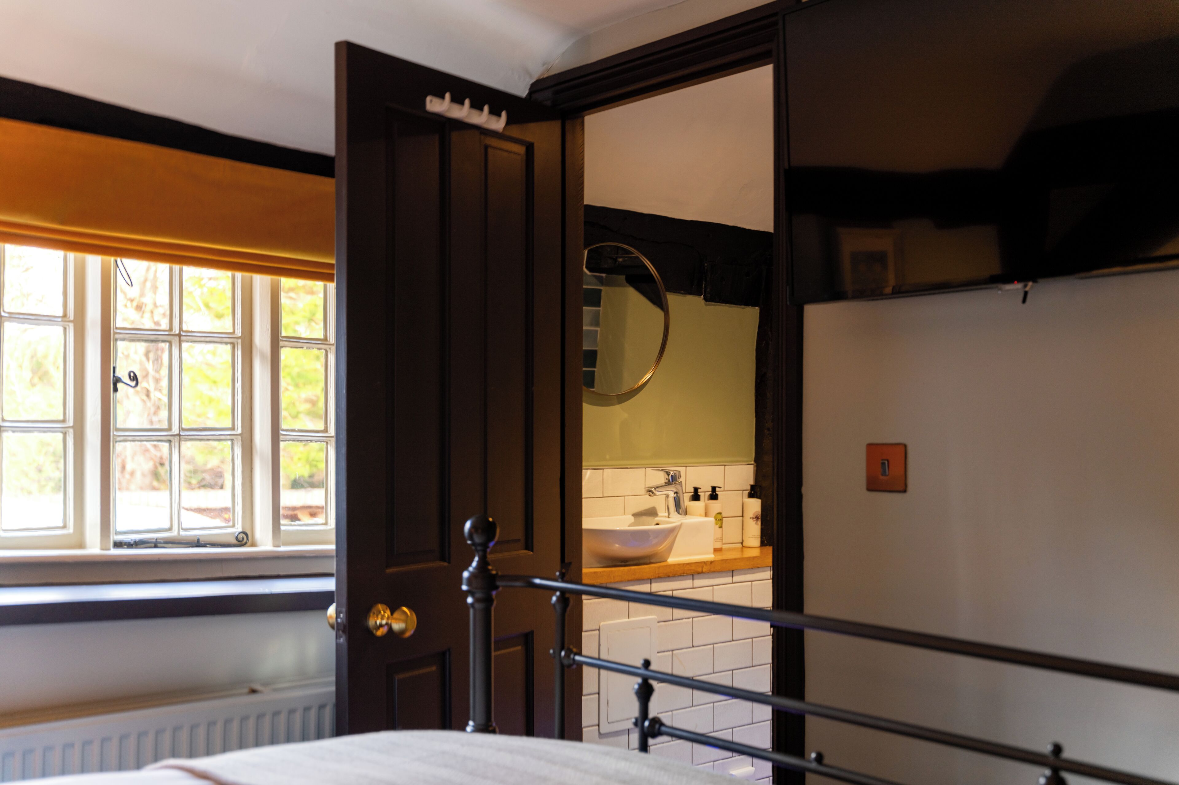 Ein Schlafzimmer mit Bett, Fenster, Badezimmer mit Waschbecken und Spiegel sowie einer Tür.