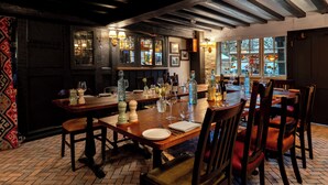 Un restaurante con mesas y sillas de madera, una zona de bar con estantes llenos de botellas, y vistas a la calle a través de amplios ventanales.