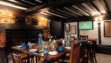Egy étkező, melynek egyik fala téglából van, a mennyezetén pedig fagerendák találhatók, és egy televízión a „The Bull Inn” logója látható.
