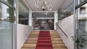 A modern staircase with a red carpet, wooden steps, and a chandelier.