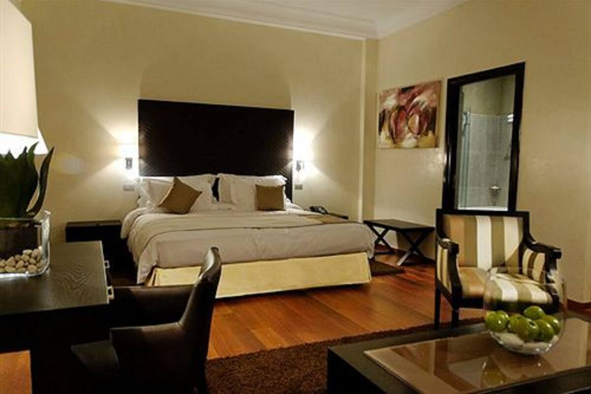 Een slaapkamer met een bed, nachtkastjes, een stoel, een tafel met een fruitschaal en een spiegel.