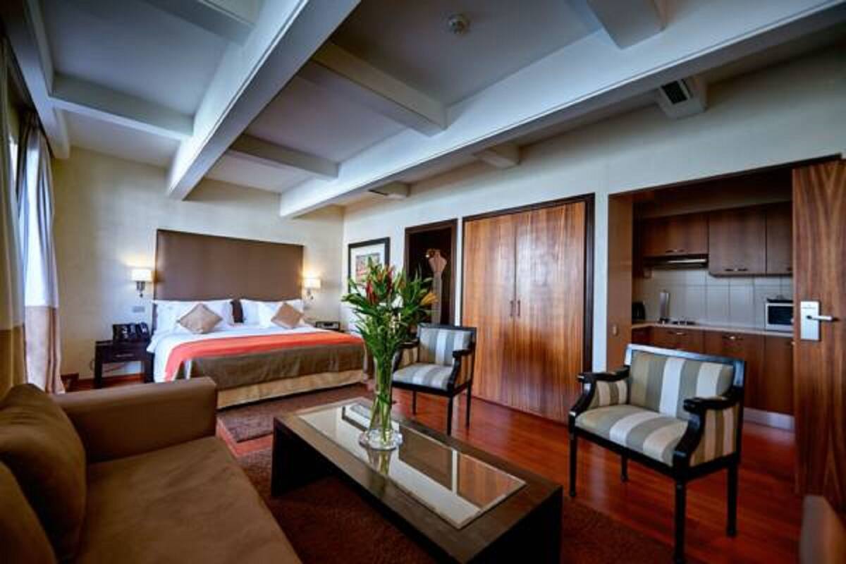 Een hotelkamer met een bed, een zithoek met een salontafel, een bank en uitzicht op de keuken.