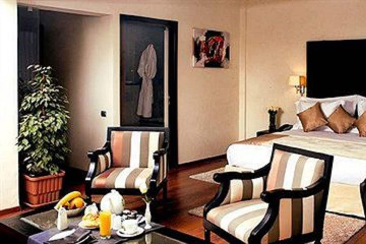 Een hotelkamer met een groot bed, twee fauteuils, een tafeltje met ontbijtartikelen, een potplant en een schilderij aan de muur.