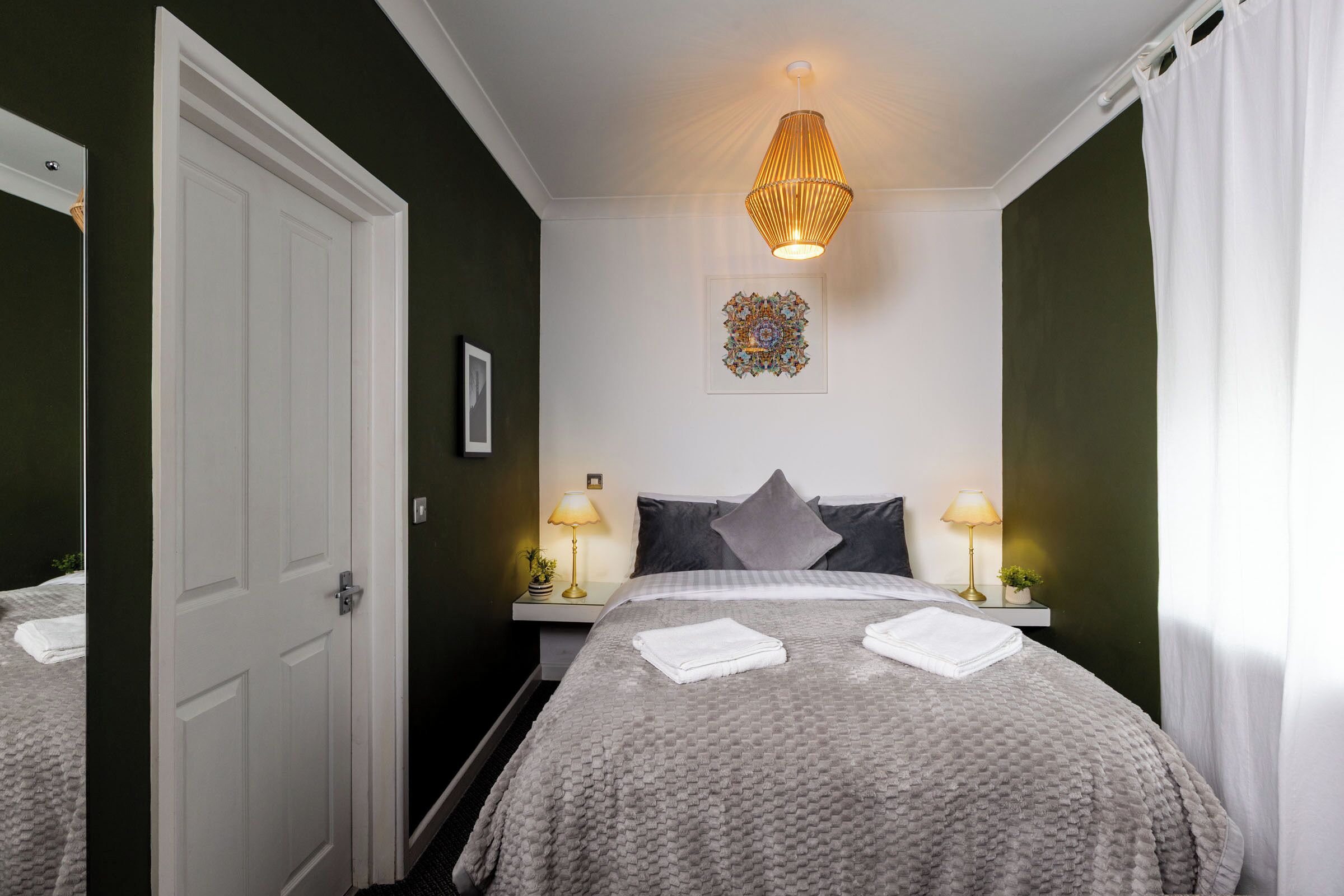 A bedroom with a bed, two bedside tables with lamps, a door, and a wall decoration.