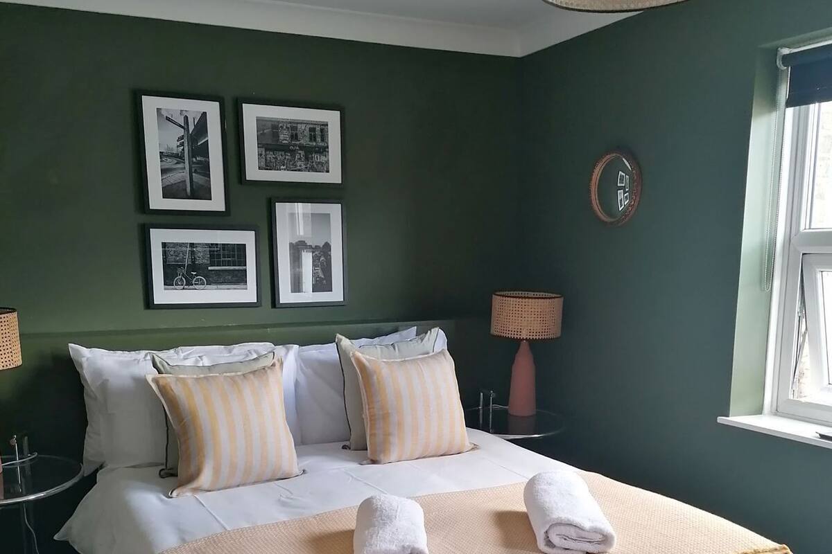 Una cama bien hecha con almohadas, una lámpara de noche y cuadros en la pared.