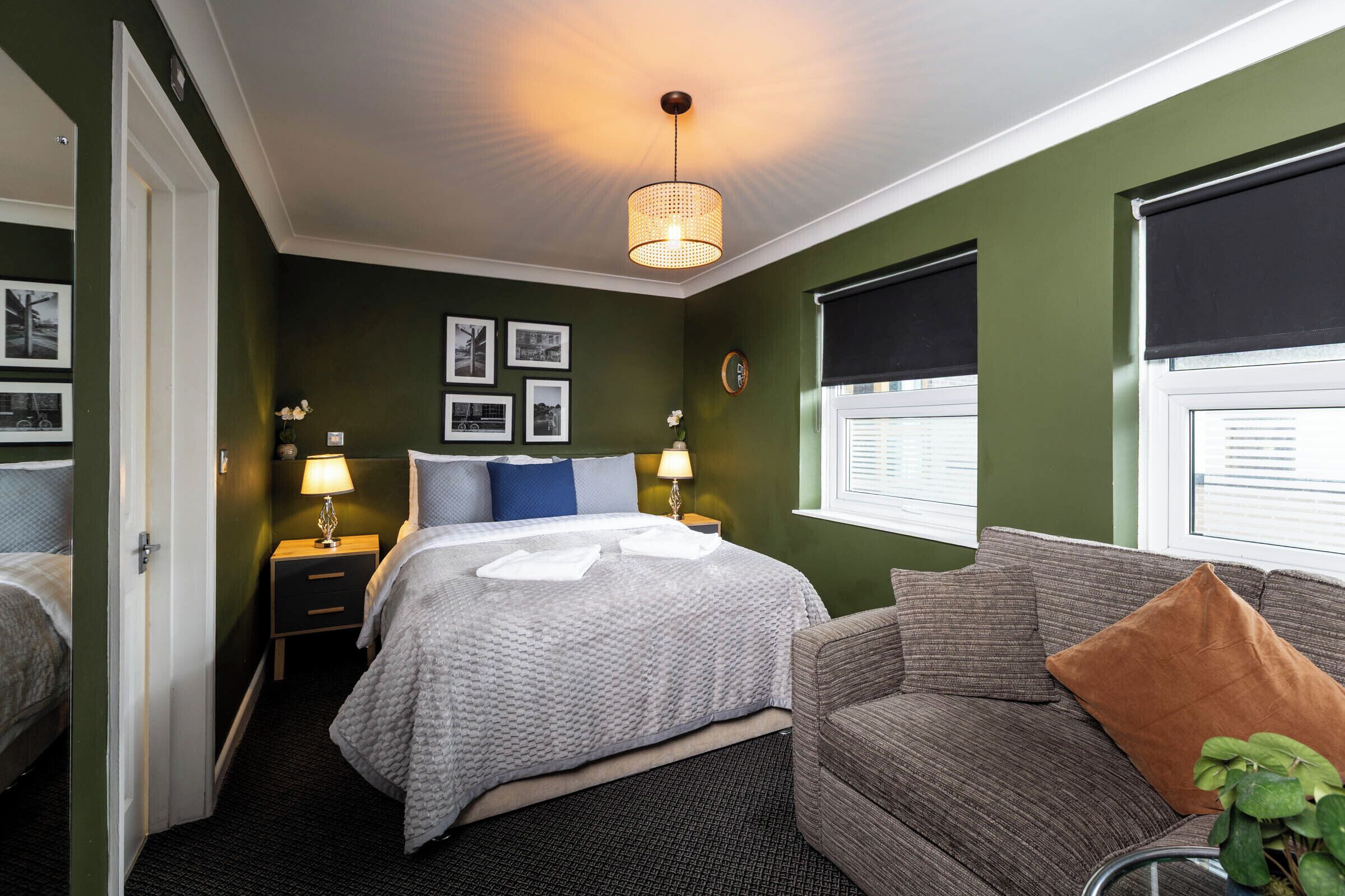 Habitación de hotel con cama, sofá, mesita de noche, lámpara y una pared con cuadros.