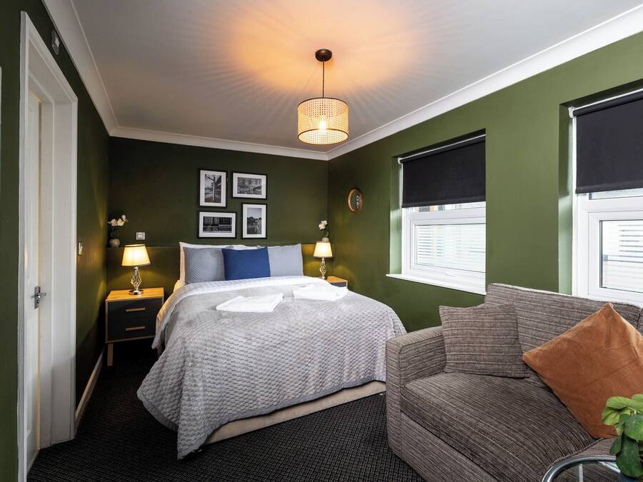 A hotel room with a bed, a sofa, a nightstand, a lamp, and a wall with framed pictures.