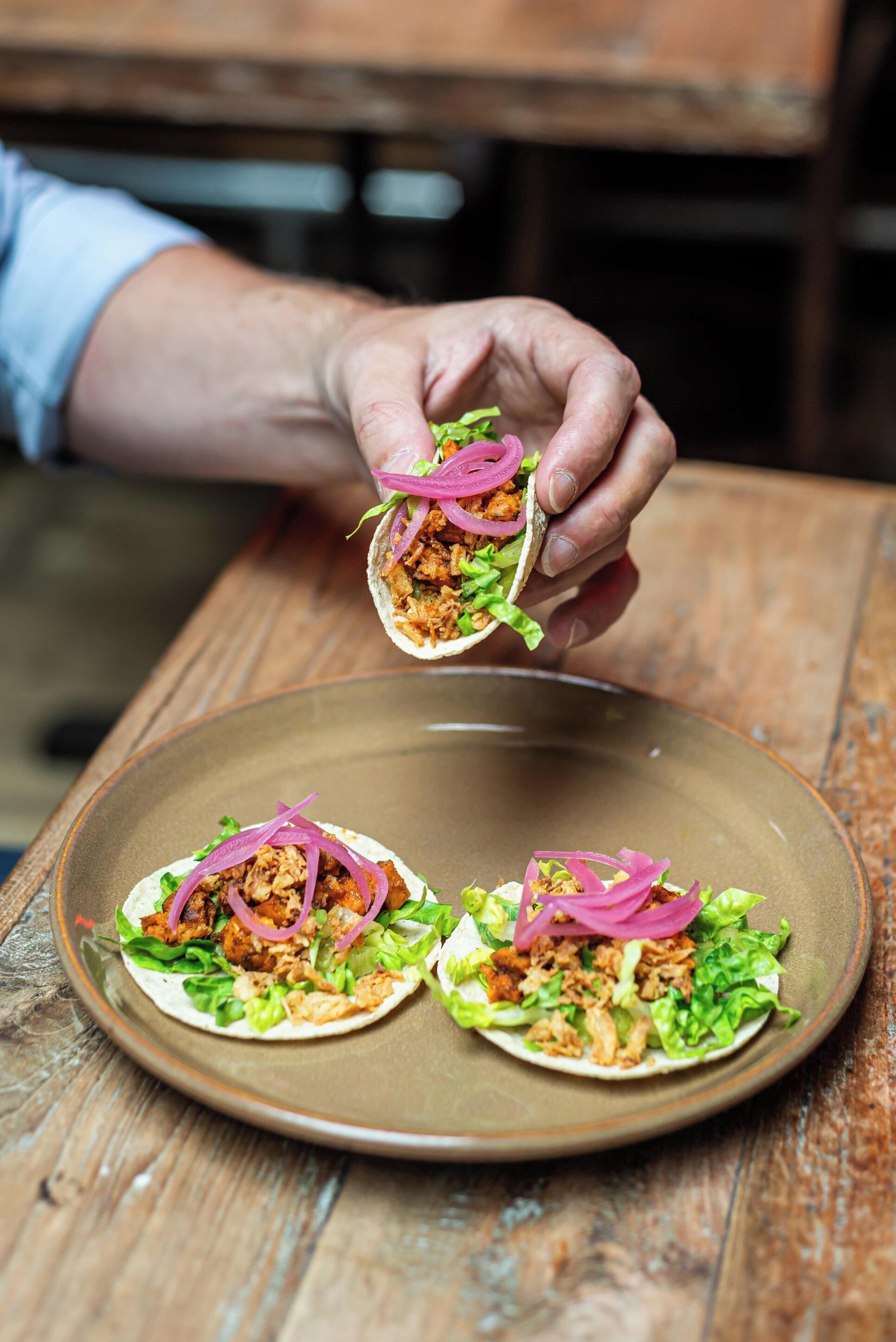 Un piatto con tre tacos su un tavolo di legno.