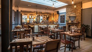 Un restaurant avec des tables et des chaises en bois, un coin bar et un mur en pierre agrémenté d’une cheminée.