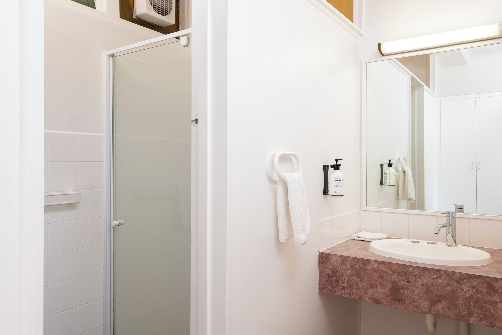 A bathroom with a glass door shower, a sink with a marble countertop, and a mirror with a towel hanging on the wall.