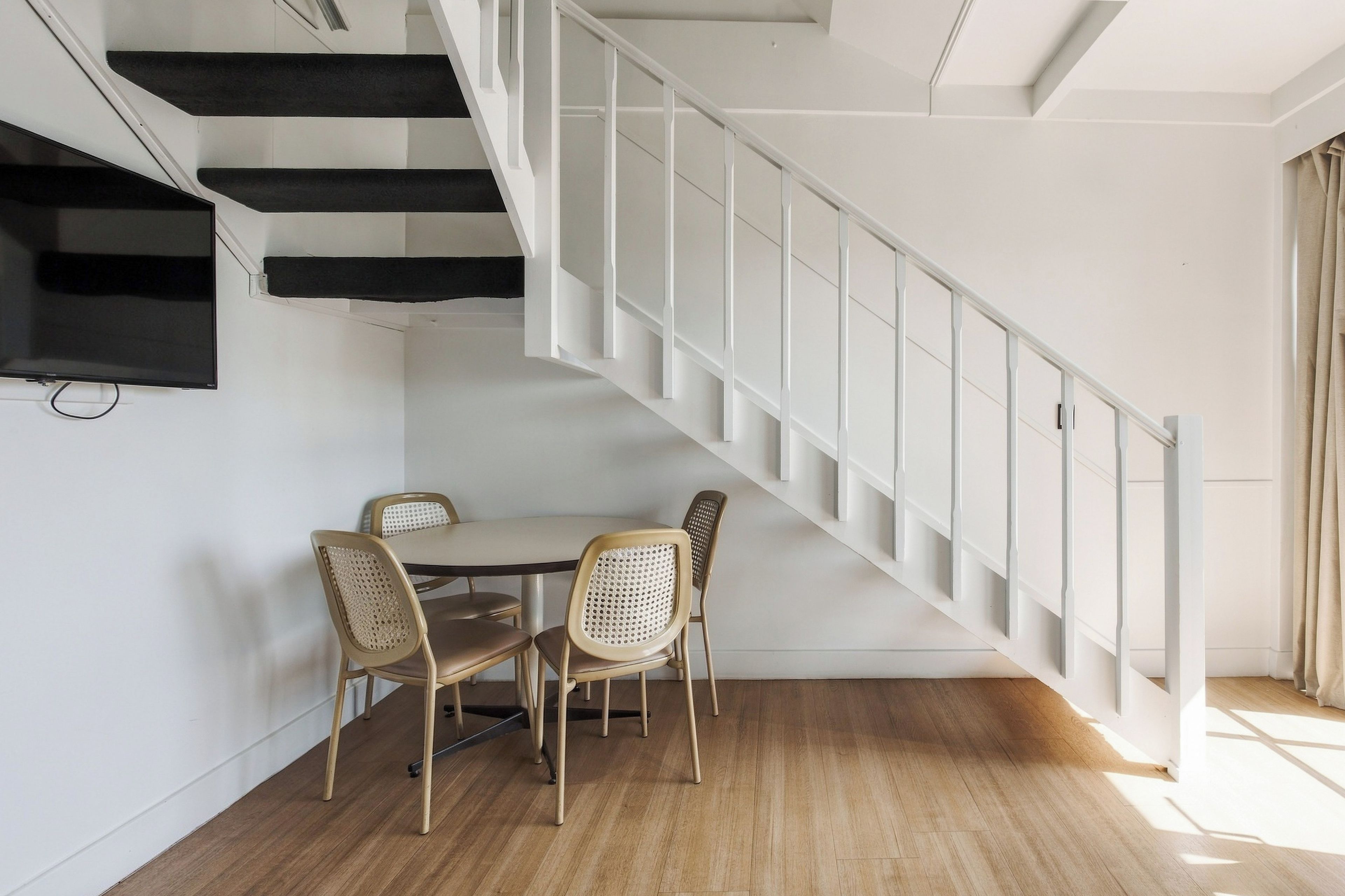 A room with a wooden floor, a white staircase, and a dining area with four chairs and a table.