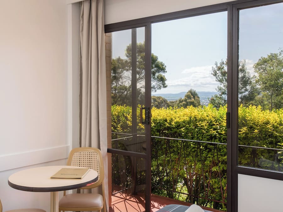 A balcony with a table and chairs, a view of greenery and distant hills.