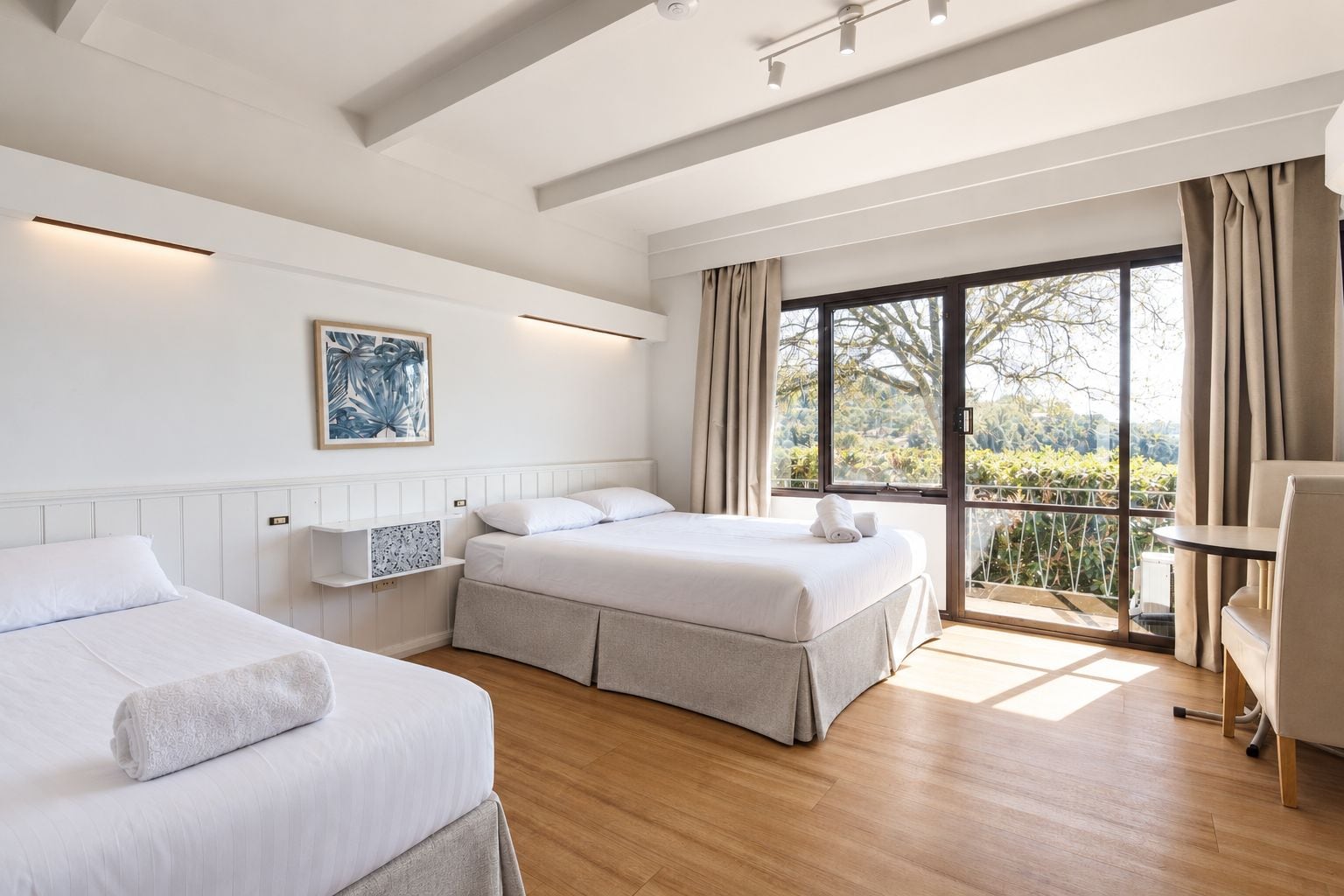 A hotel room with two beds, a desk, and a large window with curtains.