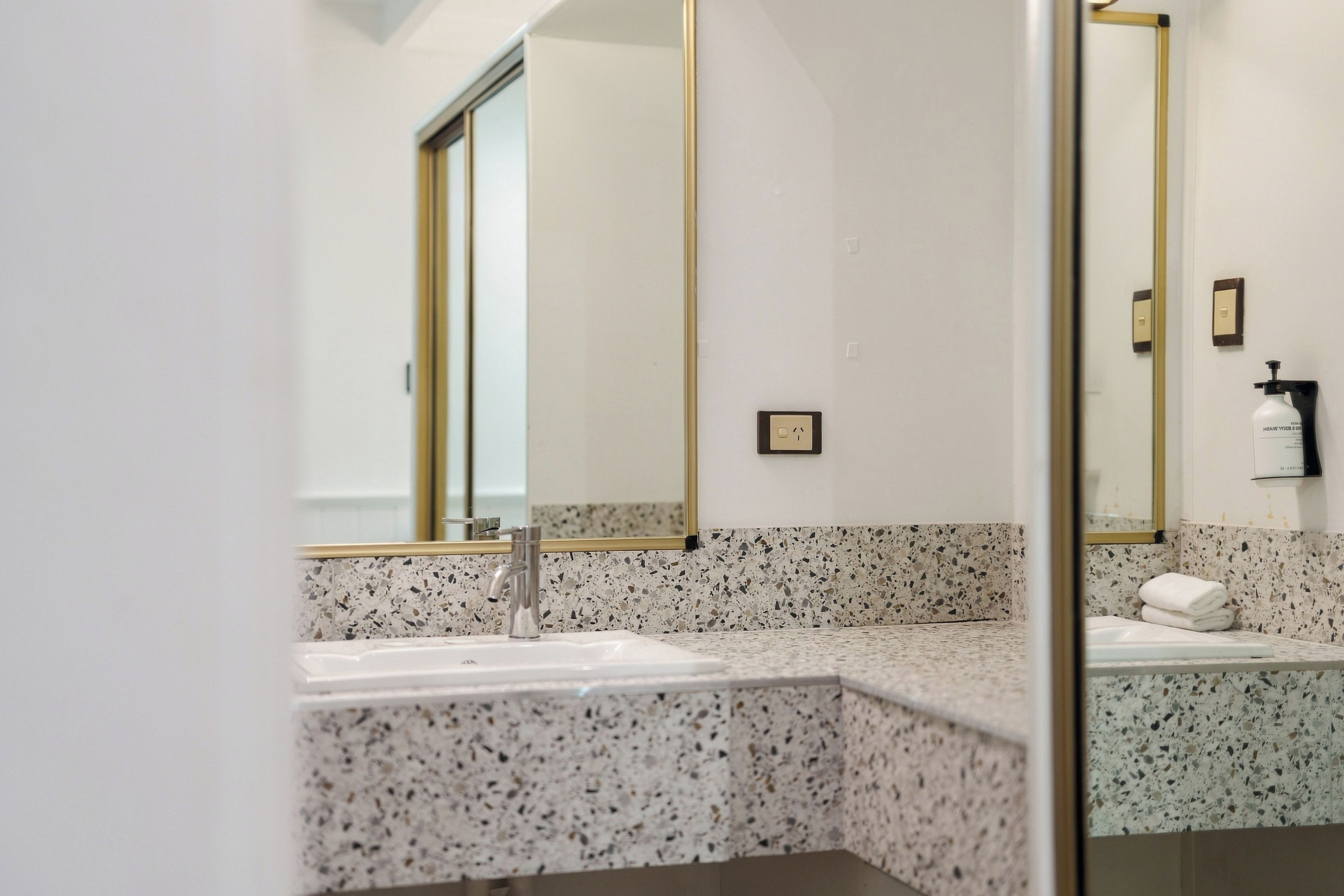 A modern bathroom with a granite countertop, a large mirror, and a towel rack.