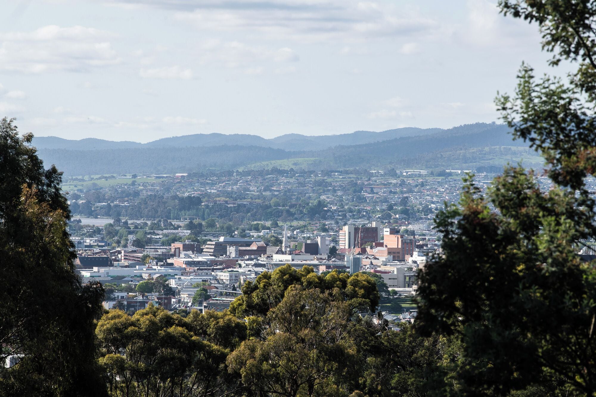A cityscape with a mix of modern and older buildings, surrounded by hills and trees.