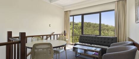 A modern room with a dining table, chairs, a sofa, and a large window offering a view of greenery.