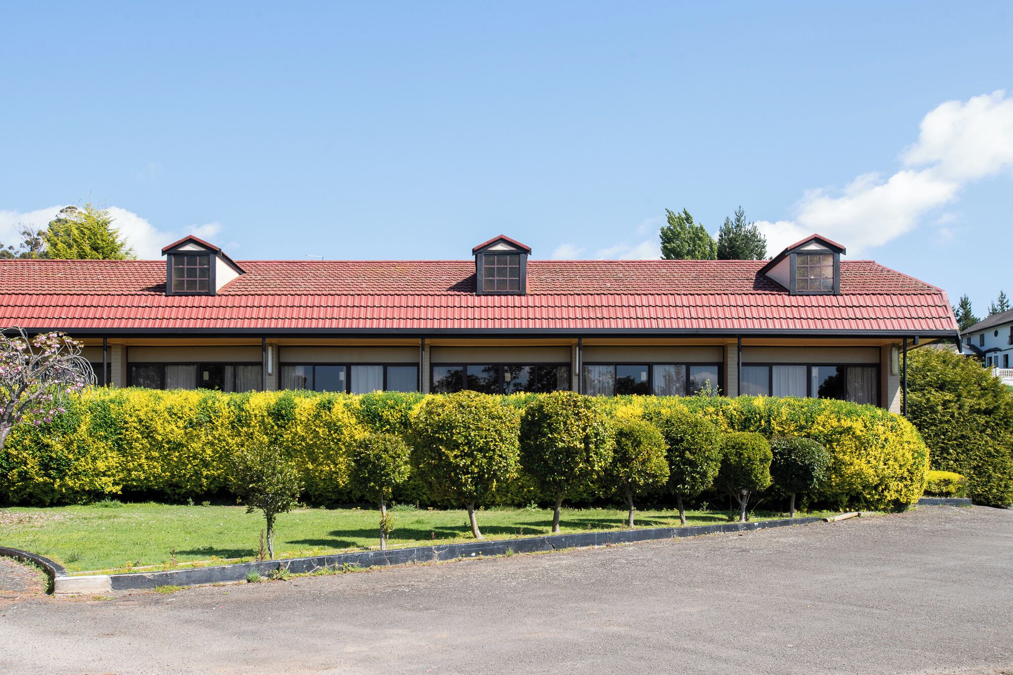 A two-story building with a red-tiled roof, multiple windows, and a well-maintained hedge in front.
