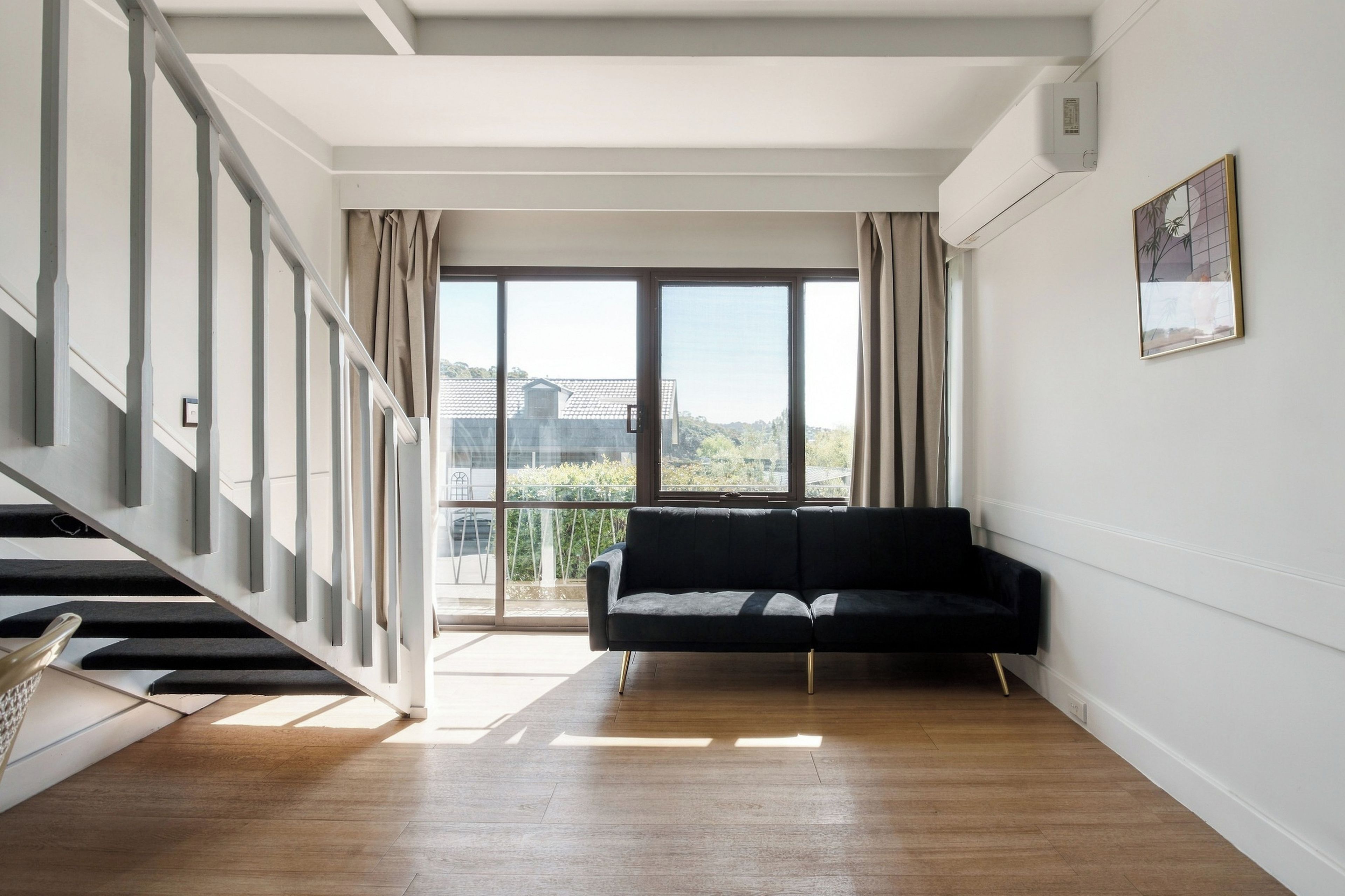 Un espacio habitable amplio con un sofá negro, una escalera y un gran ventanal con vistas a la ciudad.