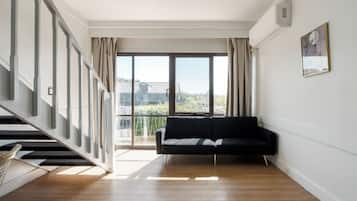 Un espacio habitable amplio con un sofá negro, una escalera y un gran ventanal con vistas a la ciudad.
