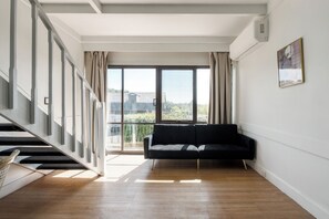 A spacious living area with a black sofa, a staircase, and a large window offering a view of the cityscape. - Village Family Motor Inn (South Launceston)