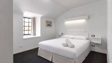 A modern hotel room with a large bed, a window with curtains, a bedside table, and a wall-mounted light fixture.