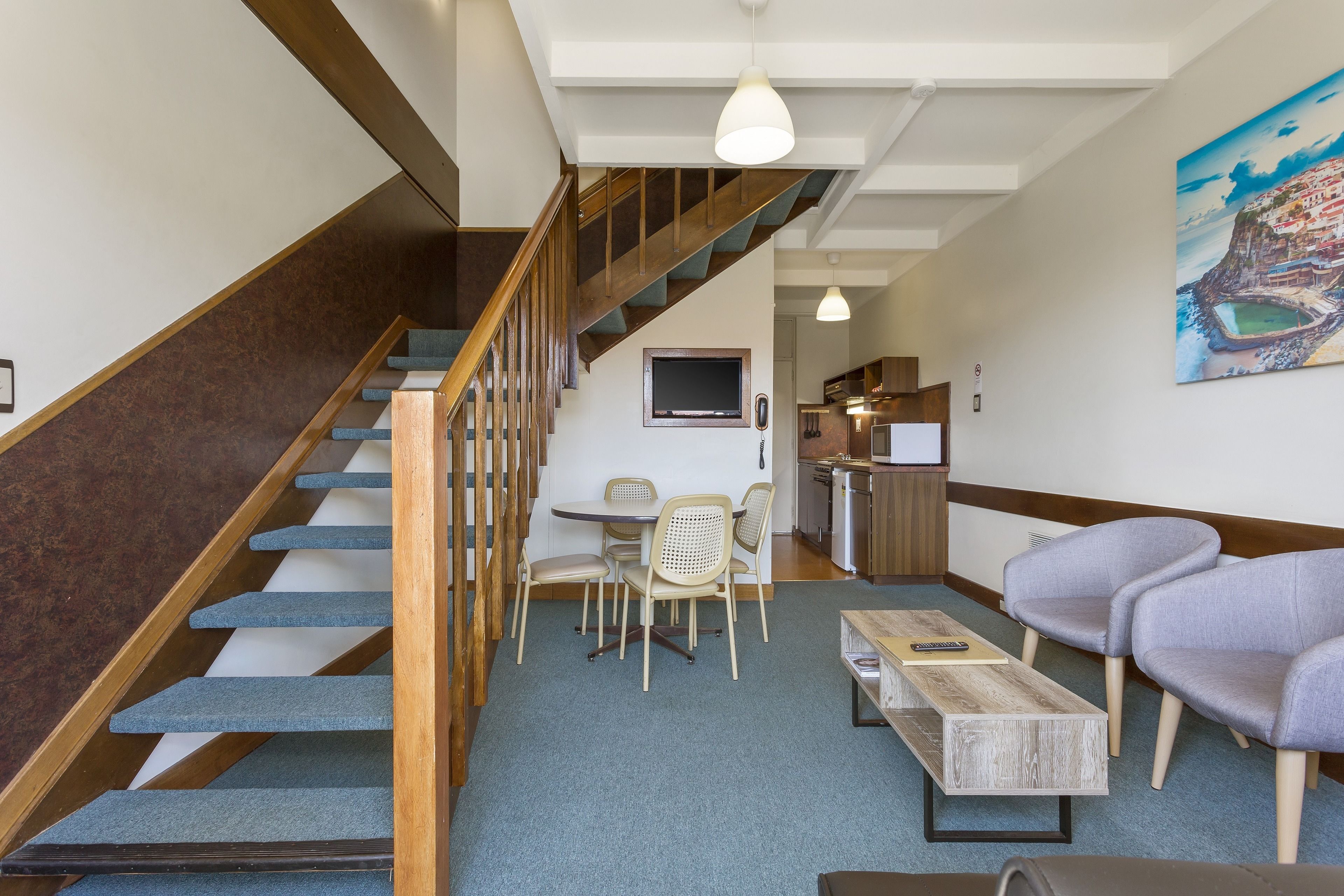 A staircase with wooden steps and a handrail, leading to a dining area with a table and chairs.