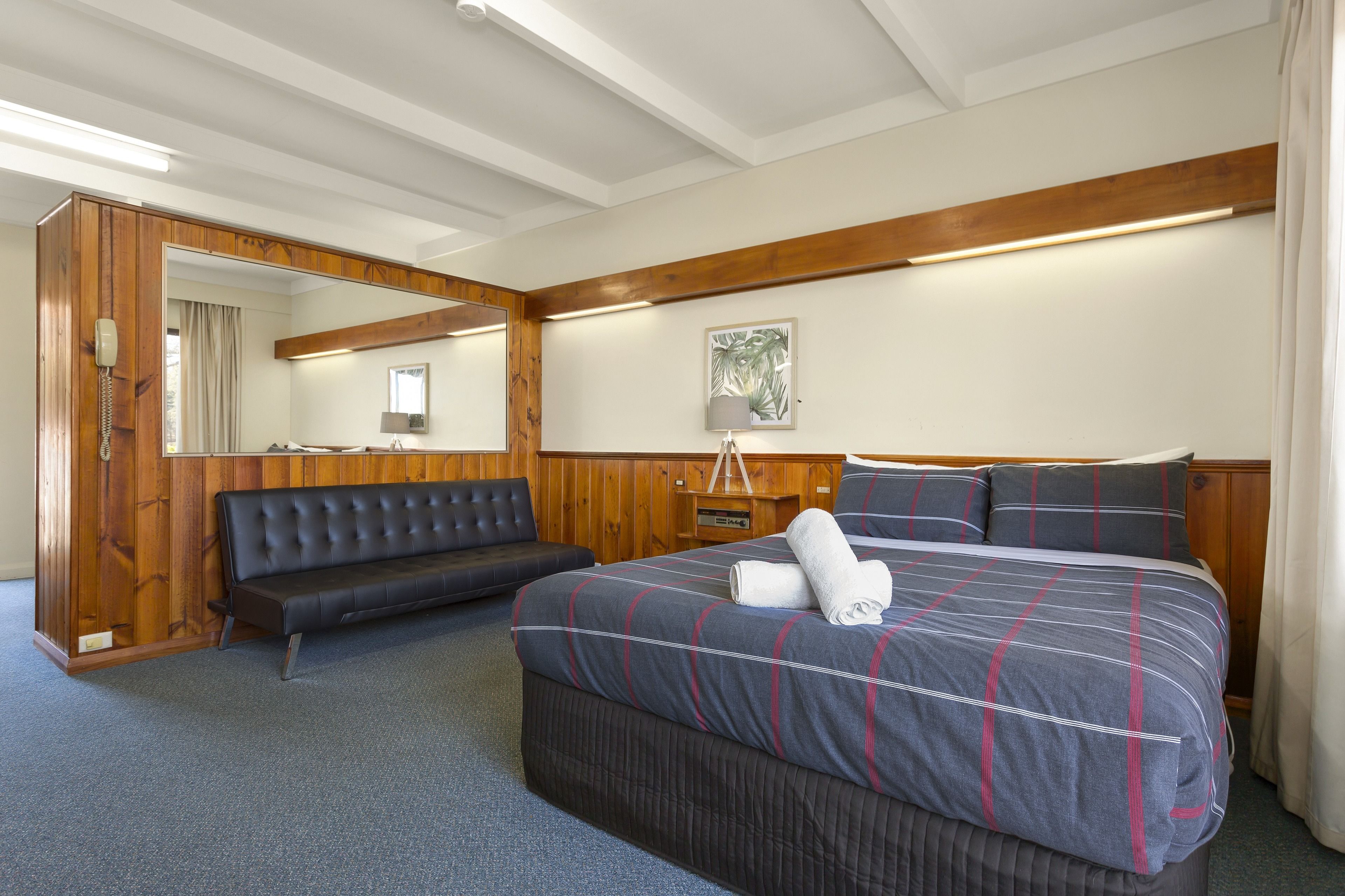 A hotel room with a large bed, a sofa, a wooden ceiling, and a mirror.
