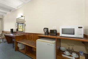 Habitación de hotel con escritorio de madera, refrigerador, microondas, cafetera y ventana con vista a árboles.